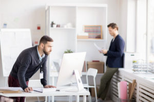 Men standing up while looking at computer screen